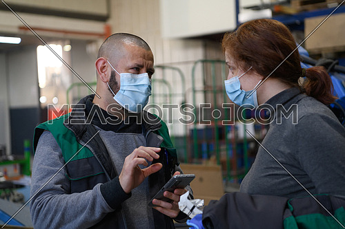 Industrial workers with face masks protected against coronavirus discussing production in the factory. People working during COVID-19 pandemic. High quality photo