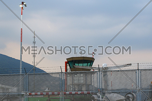 Small international airport control tower with jet airplane and security fence and lights