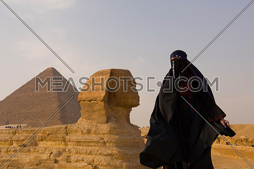 egyptian woman in traditional clothes in front of ancient grea giza pyramids  and sphinx profile