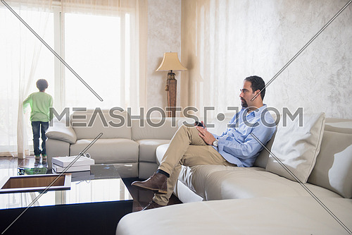 Middle Eastern father cheerfully spends time with his son on the sofa and enjoy watching tv