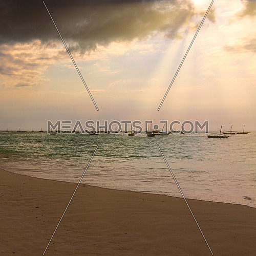 Several fishing boats silhouette anchored out in the ocean off the coast of Zanzibar, at sunset with sunbeams.