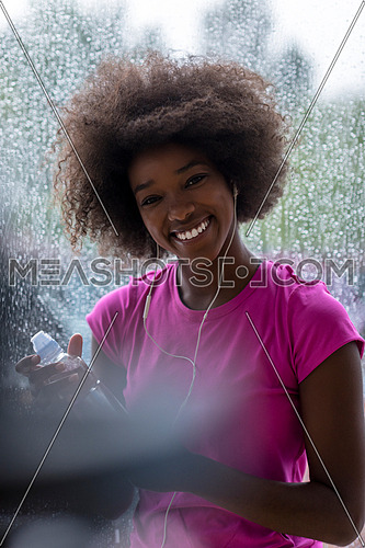 portrait of young afro american woman in gym on work out break while teaking breath and fresh water rainy day and bad weather outdooor