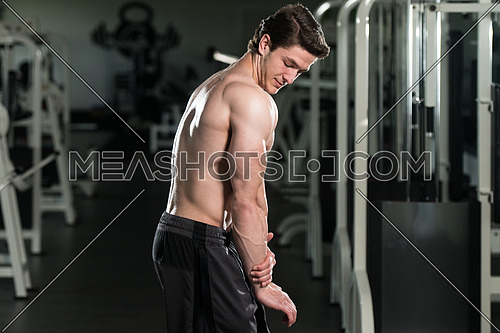 Young Man Standing Strong In The Gym And Flexing Side Triceps Pose - Muscular Athletic Bodybuilder Fitness Model Posing Exercises