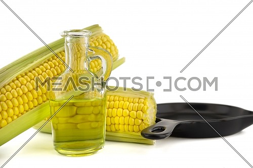 Corn oil in decanter and fresh corncobs next to the cast iron skillet isolated on white background with free copy space for text