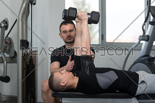 Personal Trainer Showing Young Man How To Train Triceps Exercise With Dumbbell In A Health And Fitness Concept