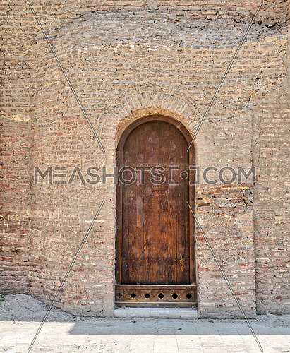 Grunge wooden aged vaulted door on exterior stone bricks wall of Amr Ibn Al-As, Medieval Cairo, Egypt
