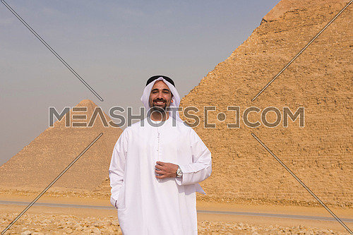 young man as tourist  wearing  arabian traditional clothes in egypt with giza pyramids in background