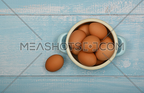 Close up metal pan bowl of brown chicken eggs on light blue rustic wooden table surface, elevated top view, directly above