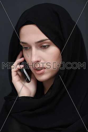 Young muslim businesswoman in traditional clothes or abaya talking on the smartphone. Arab woman  in front of black chalkboard and representing techology, islamic  fashion and Ramadan kareem concept