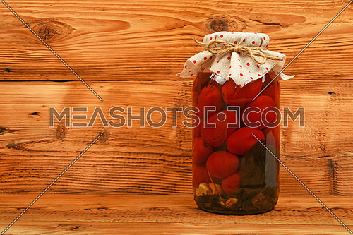 One big glass jar of homemade pickled tomatoes with dotted textile top decoration at brown vintage wooden surface