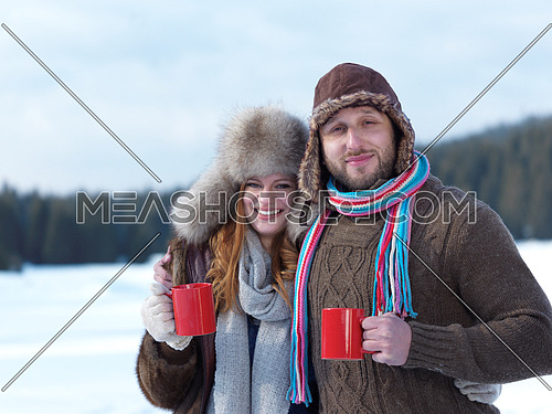 portrait of happy young couple outdoor on winter day drinking warm tea with fresh snow in background