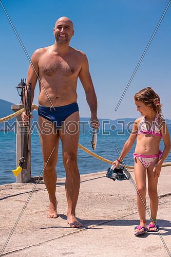 Young smiling fisherman with his little daughter carrying freshly caught fish after underwater fishing  active holiday concept
