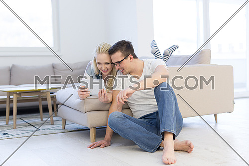 Young couple relaxing at  home using tablet computers reading in the living room on the sofa couch.