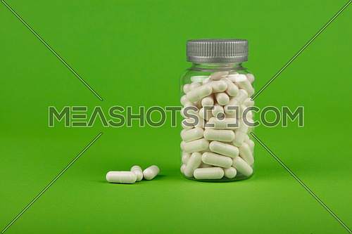 Close up one bottle of white gel cap pills of medicine over natural green background with copy space, low angle side view
