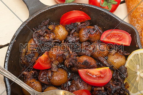 Baby cuttle fish roasted on iron skillet with tomatoes and onions over rustic wood table
