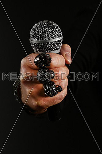Close up man hand with metal rings and bracelet holding microphone over black background, side view