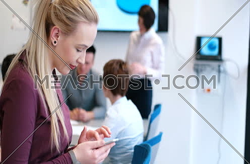 Zoom out for Elegant Blond Woman Using Mobile Phone in office interior at day.