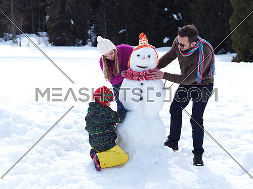 happy young  family playing in fresh snow and making snowman at beautiful sunny winter day outdoor in nature with forest in background