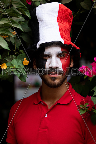 An Egyptian male painted Egyptian flag on his face with a hat on his head
