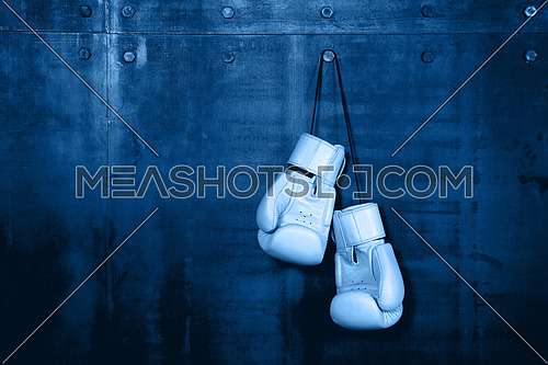 Close up pair of clasic white leather boxing gloves hanging over dark blue wall with copy space