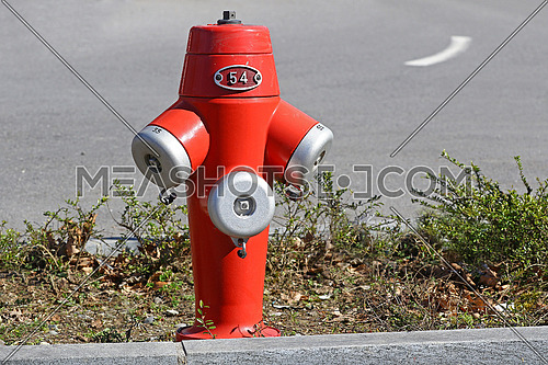 Red fire hydrant in the sun between two lanes of a city road