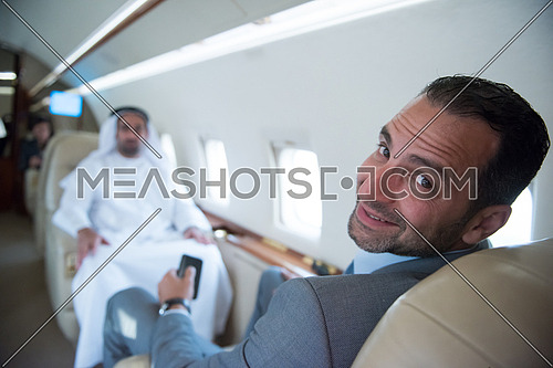 Young middle eastern successful businessman enjoyed by talking with Arab business partner while sitting in private jet