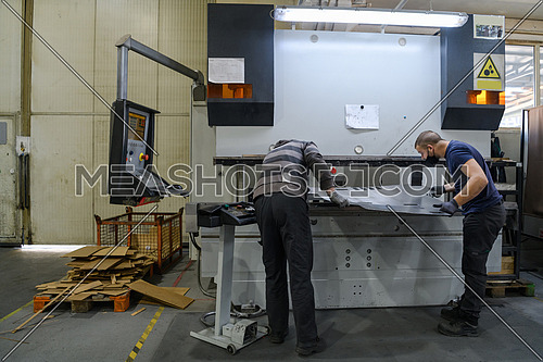 two workers wearing a protective mask due to a coronavirus pandemic, working in a modern factory, and preparing a program and materials for a CNC machine. High quality photo