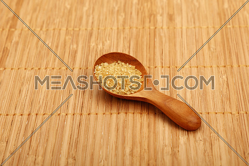 Wooden round scoop spoon of brown cane sugar on bamboo mat background
