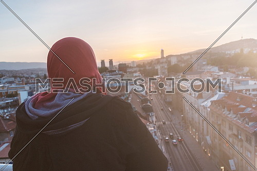 Muslim woman in hijab looking sunset sky on city landscape