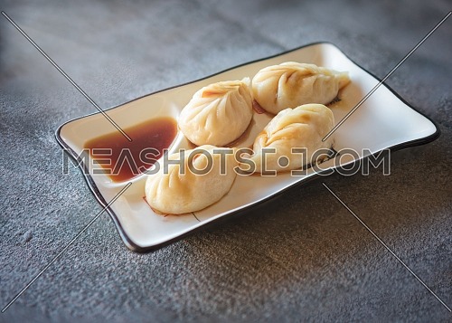 chinese steamed rolls served on rectangular white plate on dark gray stone background