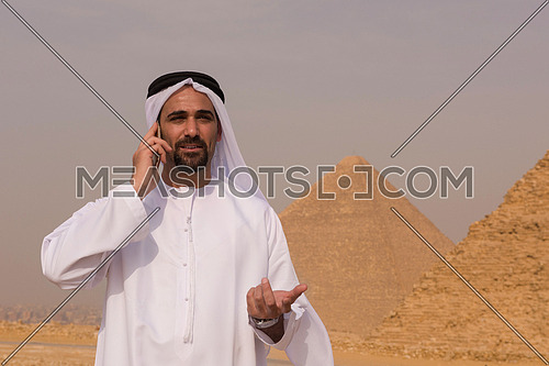 young middle eastern businessman  speeking by phone with egyptian giza pyramids in background