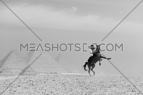 black and white image of young Egyptian man horse rearing in desert giza platue with the pyramids in background