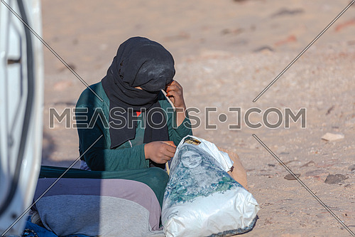 mid Shot for a bedouin woman sits on sands from Sinai Trail at day.