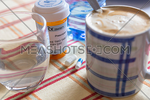 Medication during breakfast, capsules next to a glass of water, conceptual image, horizontal composition