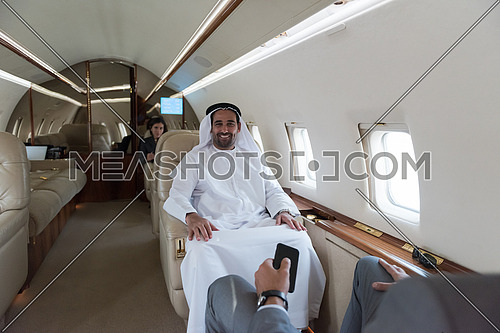 Portrait of a young middle eastern successful man in traditional clothes who enjoys sitting in private jet