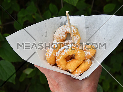 Woman hand holding portion of fresh small mini ring donuts with sugar in white paper parchment, close up, high angle view, personal perspective
