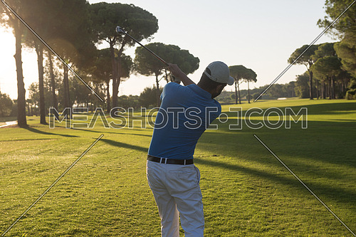 handsome sporty man, golf player hitting shot with club on course at beautiful morning
