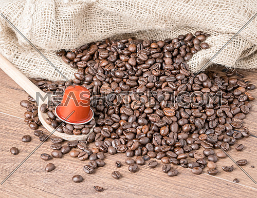 Coffee capsule on wooden spoon and roasted coffee beans with burlap sack on wooden background.