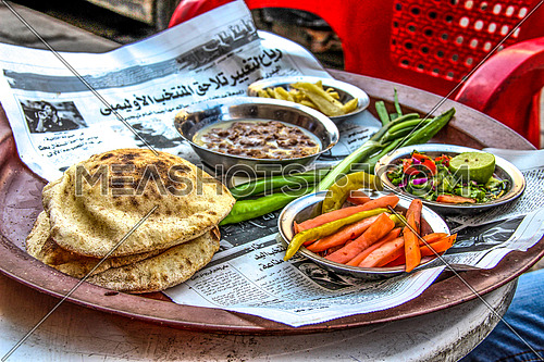 a photo for a traditional breakfast served in a street coffee shop in Cairo, Egypt showing the bread , pickles and beans