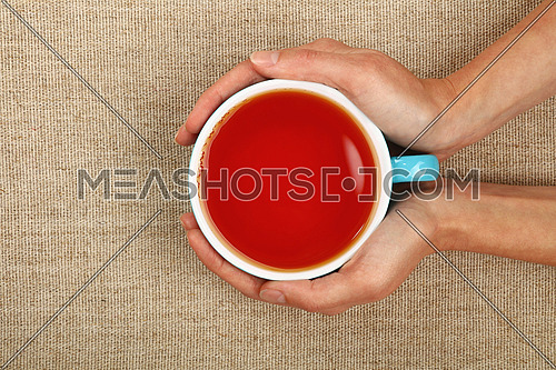 Two woman hands holding embracing big blue cup of black red over linen canvas background, warming hands