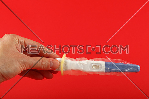 Close up woman hand holding pregnancy test with condom on it over red background with copy space, low angle side view