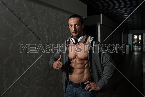Muscular Mature Man Listening Music From His Mp3 Player In Modern Corridor Where He Poses