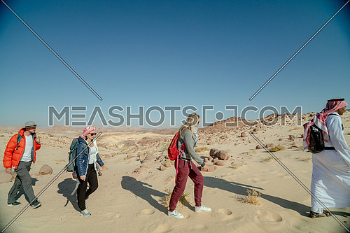 Group of tourists walking on sands with bedouin guide while exploring Sinai Trail from Ain Hodouda at day.