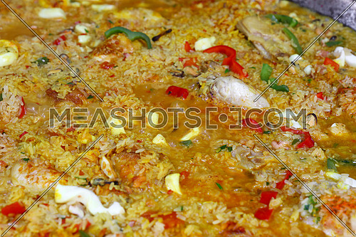 Close up cooking traditional Spanish Valencian mixed paella with chicken, seafood and vegetables in big frying pan, high angle view
