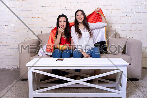 Two female friends watching TV and supporting Egyptian soccer team