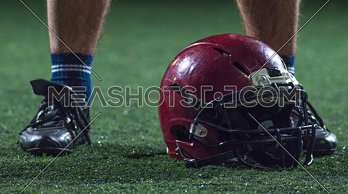 closeup shot of american football player and helmet on grass field at night