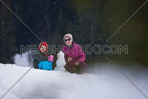 happy young  family playing in fresh snow and building snowman at beautiful sunny winter day outdoor in nature
