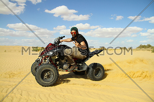 young middle eastern quad motorcycle driver enjoys driving around the desert on a sunny day