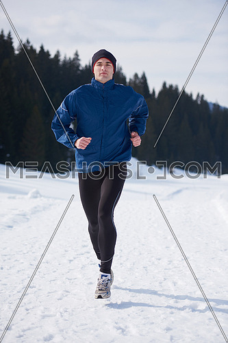 young  man jogging on snow in forest, bautiful sunny winter day. handsome sporty ahtlete man running