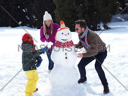 happy young  family playing in fresh snow and making snowman at beautiful sunny winter day outdoor in nature with forest in background